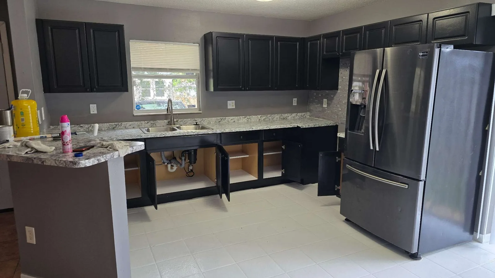 The same Tampa kitchen fully finished after the rehabilitation, with repainted black cabinets, a new granite countertop and sink and a refinished white tile floor, photographed during the final walkthrough clean
